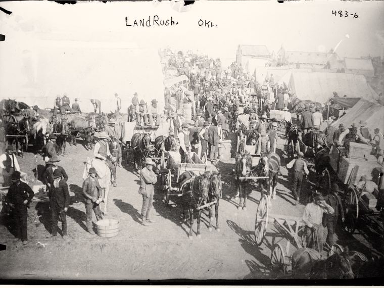 A land rush tent city of wagons and crowds, LandRush. OKL. handwritten across the sky. Library of Congress ggbain.02286.