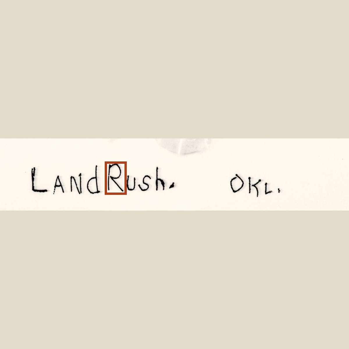 The caption LandRush. OKL. zoomed to fill the frame, with a rust rectangle around the letter R